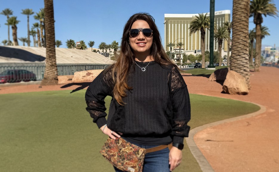 woman with long dark hair and a black shirt in front of palm trees