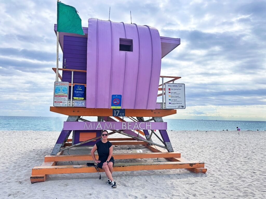 Woman sits on a bright pink lifeguard tower on a white sandy beach