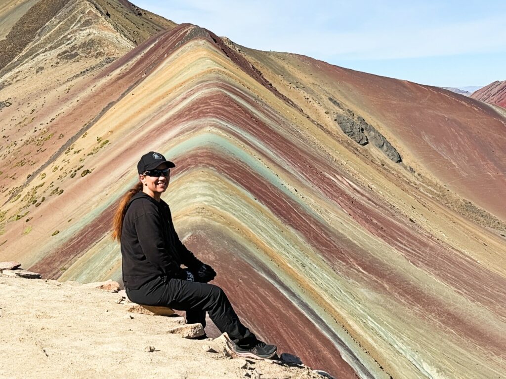 Woman wearing all black sits in front of a red and beige striped mountain